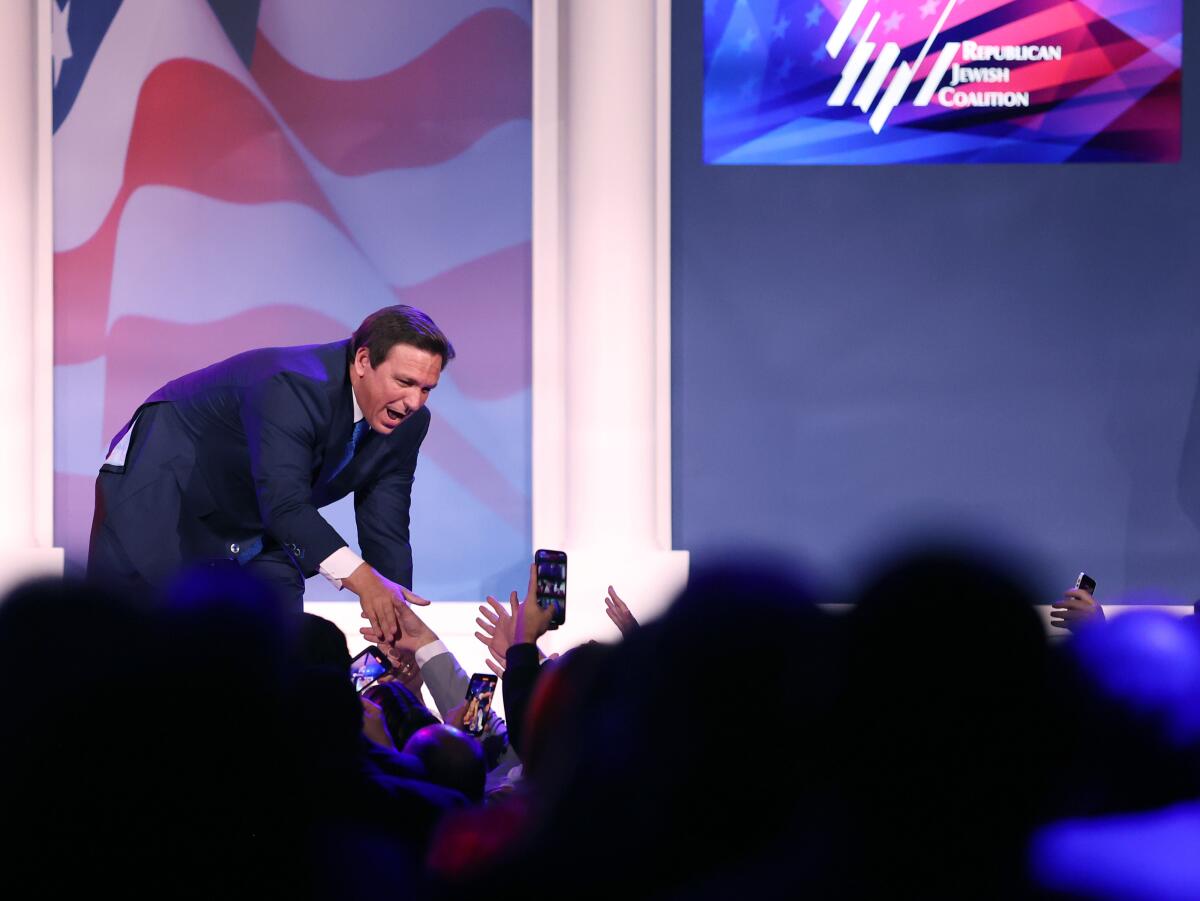 Florida Gov. Ron DeSantis pictured on a stage leaning into a crowd to shake hands at a meeting in Las Vegas