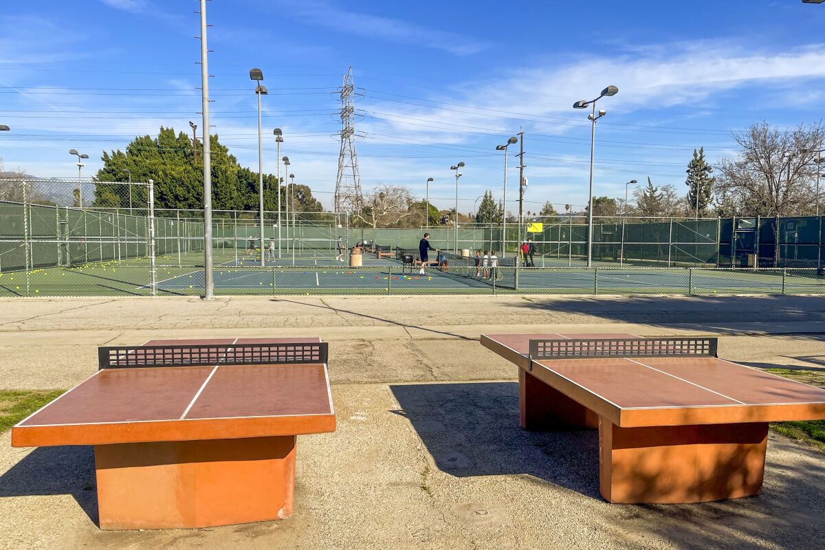 Ping pong tables sit in front of tennis courts