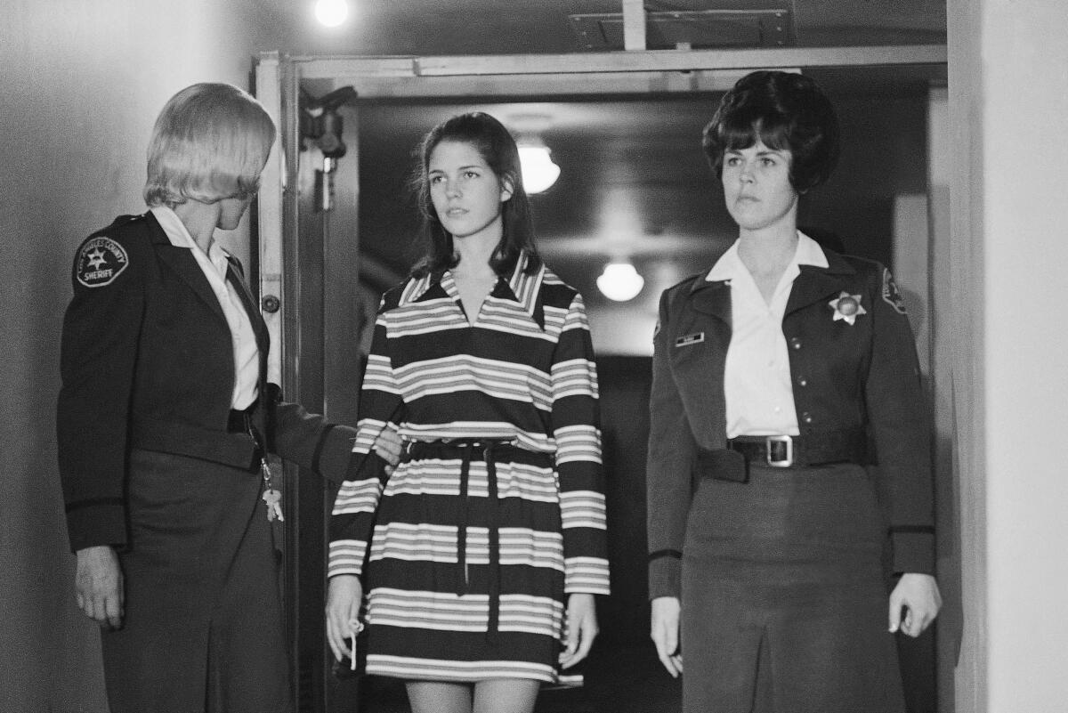 A black-and-while file photo from 1969 shows a 19-year-old Leslie Van Houten flanked by two deputy sheriffs.