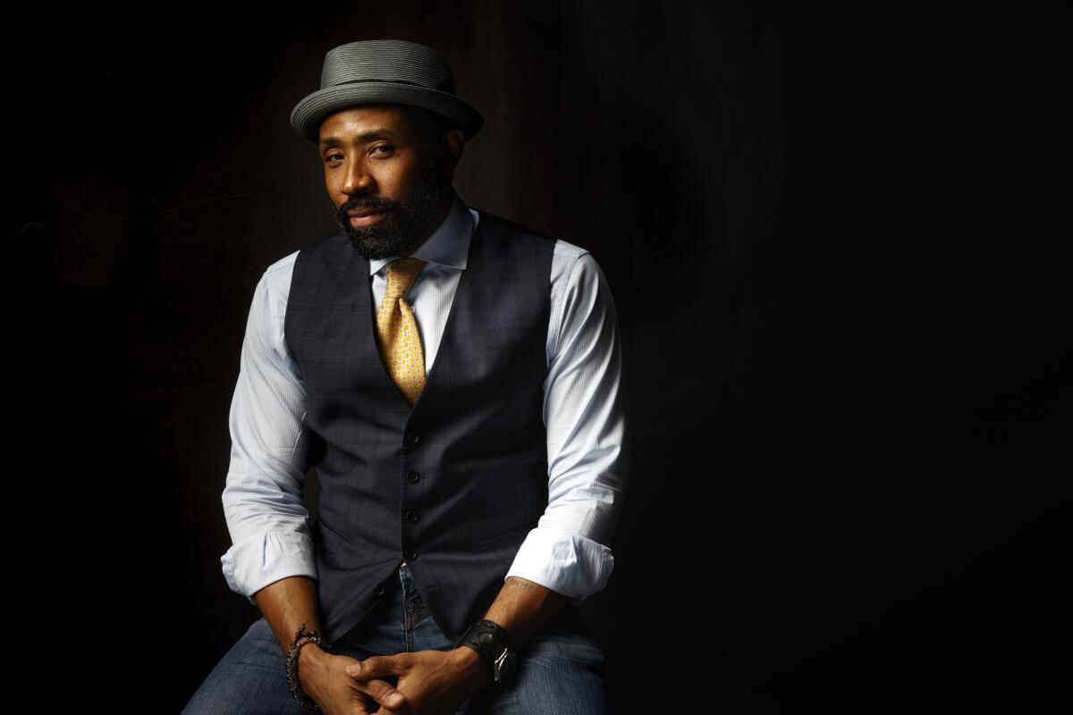 Actor Cress Williams sits for a photo portrait in porkpie hat, vest and tie. 