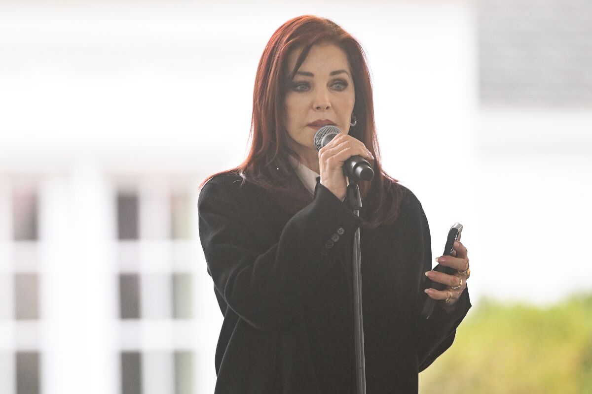 A woman with dark red hair reads a poem while holding a microphone
