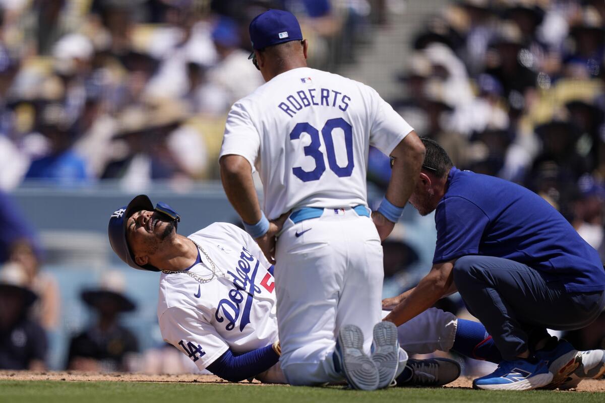 Mookie Betts, à esquerda, se contorce no chão após ser atingido por um arremesso enquanto o técnico Dave Roberts e um treinador do time observam.