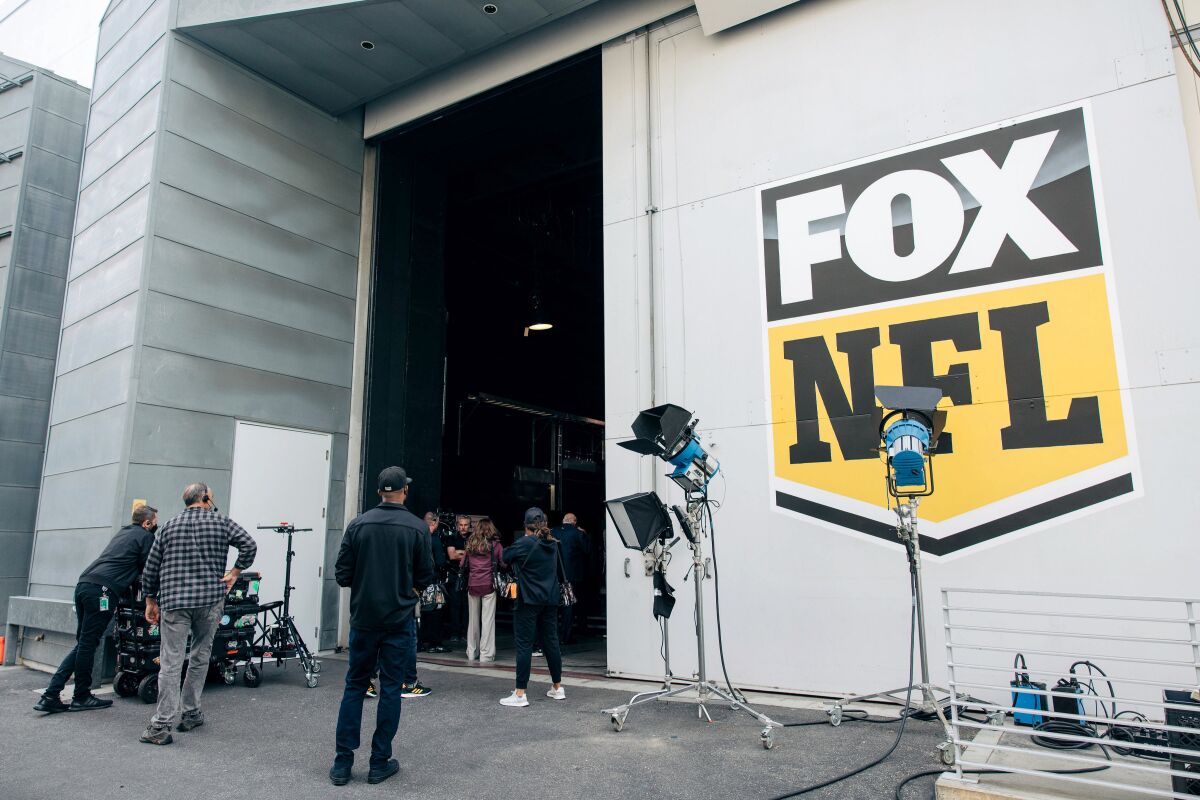 People outside a big building with the words "Fox NFL" on a wall.