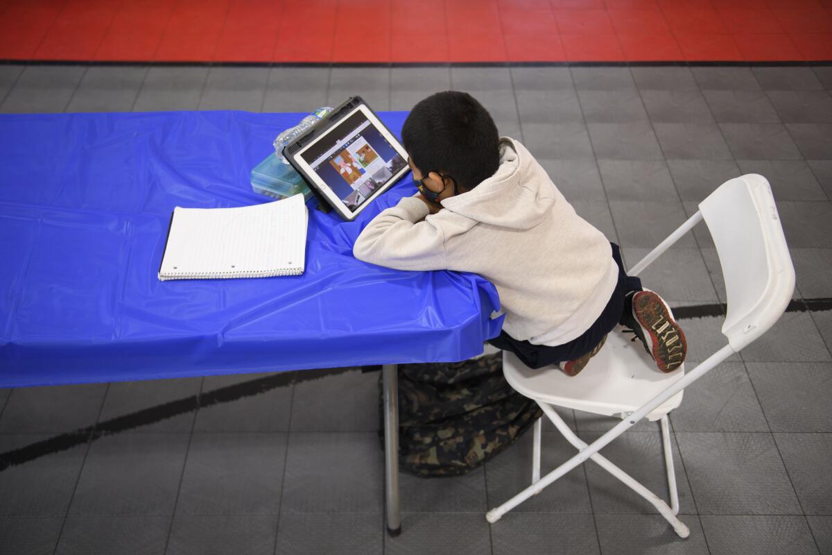A child sits at a table in front of a tablet. 