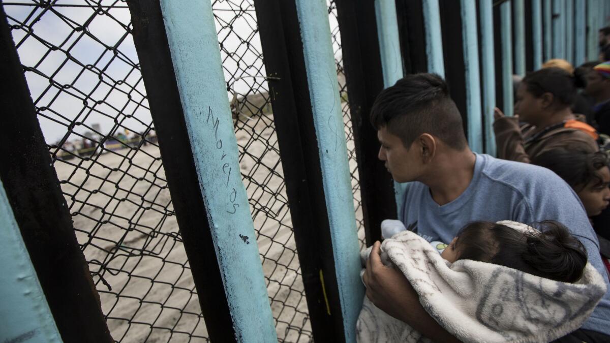 A member of the Central American migrant caravan holds a child while he looks through the border wall in Tijuana toward the United States on April 29.