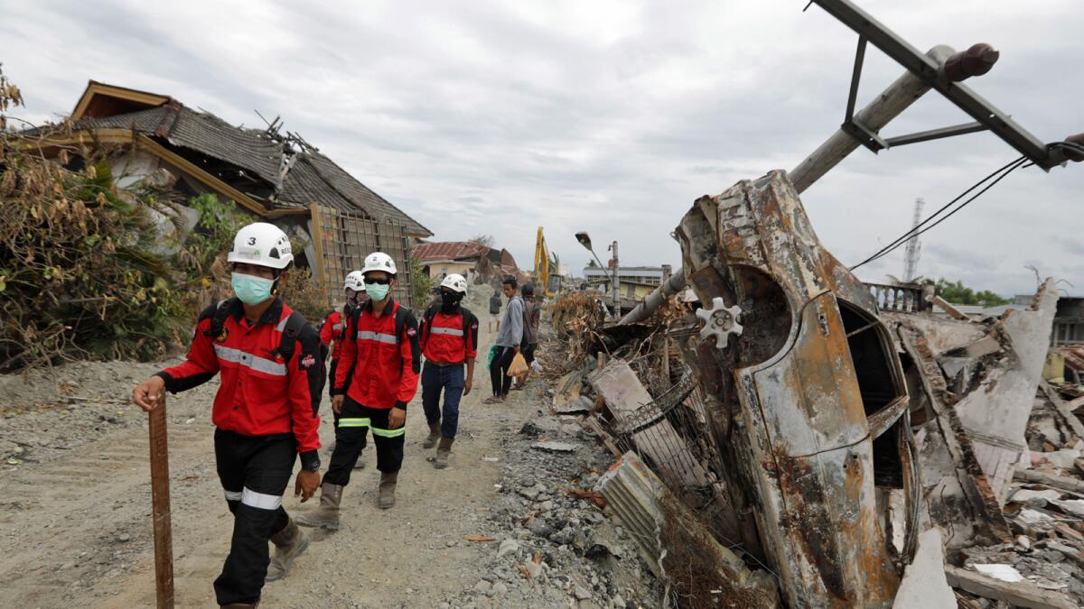 A rescue team passes a destroyed car in a devastated area of Balaroa village in Palu, Indonesia, Oct. 11.