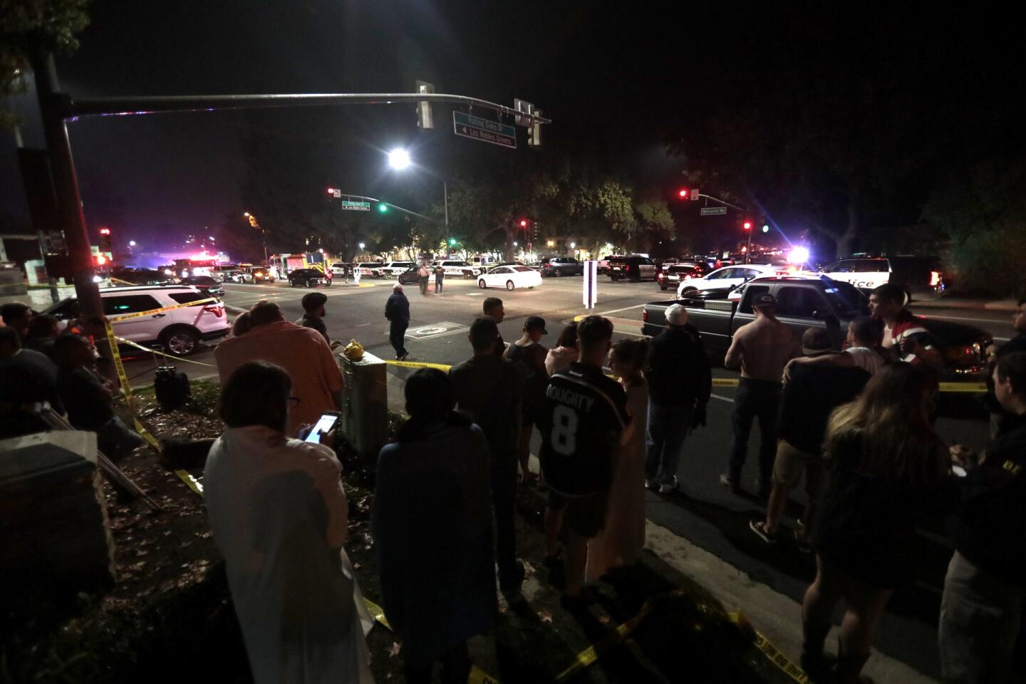 A crowd including survivors gathers at a street corner near the Borderline Bar & Grill.