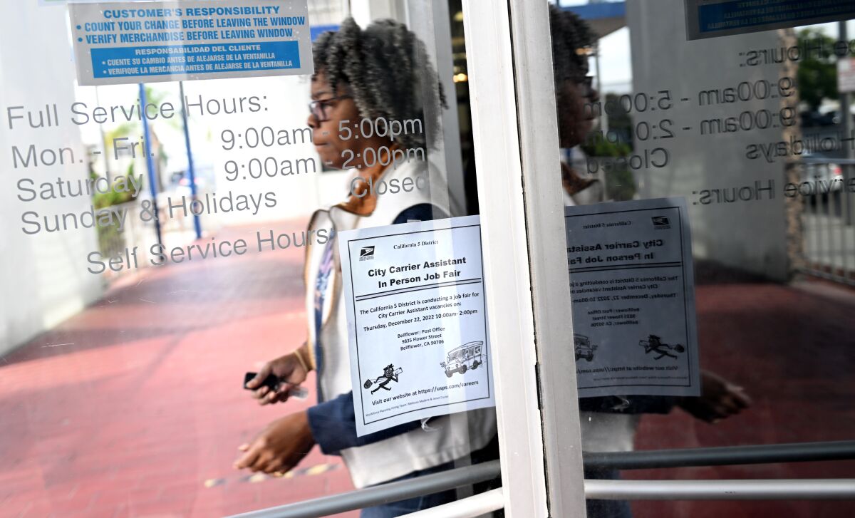 A woman passes bind a glass door, which displays opening hours and a flier for a job fair.