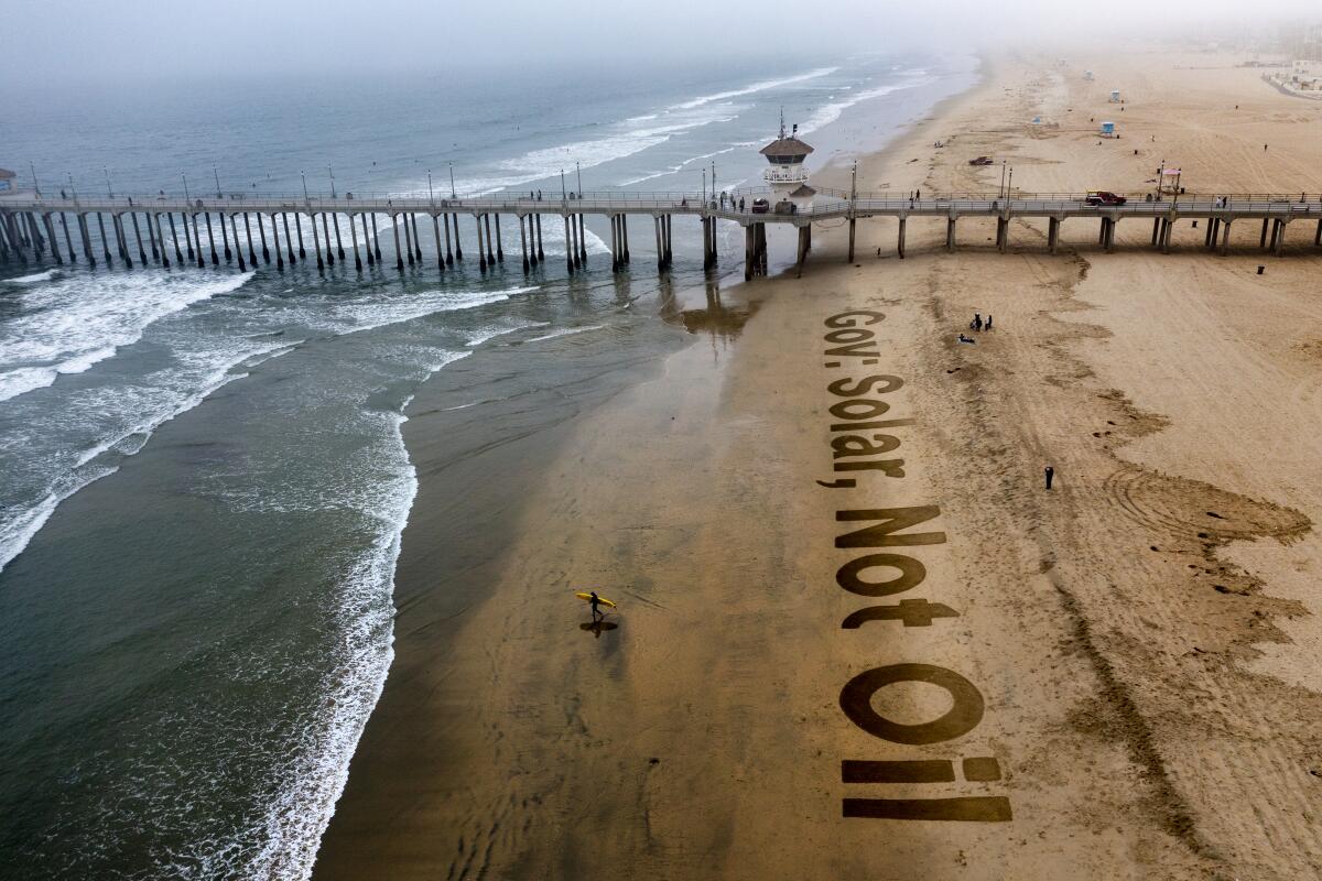 A surfer heads for the water as solar advocates finish writing a 200-foot message in the sand in Huntington Beach.