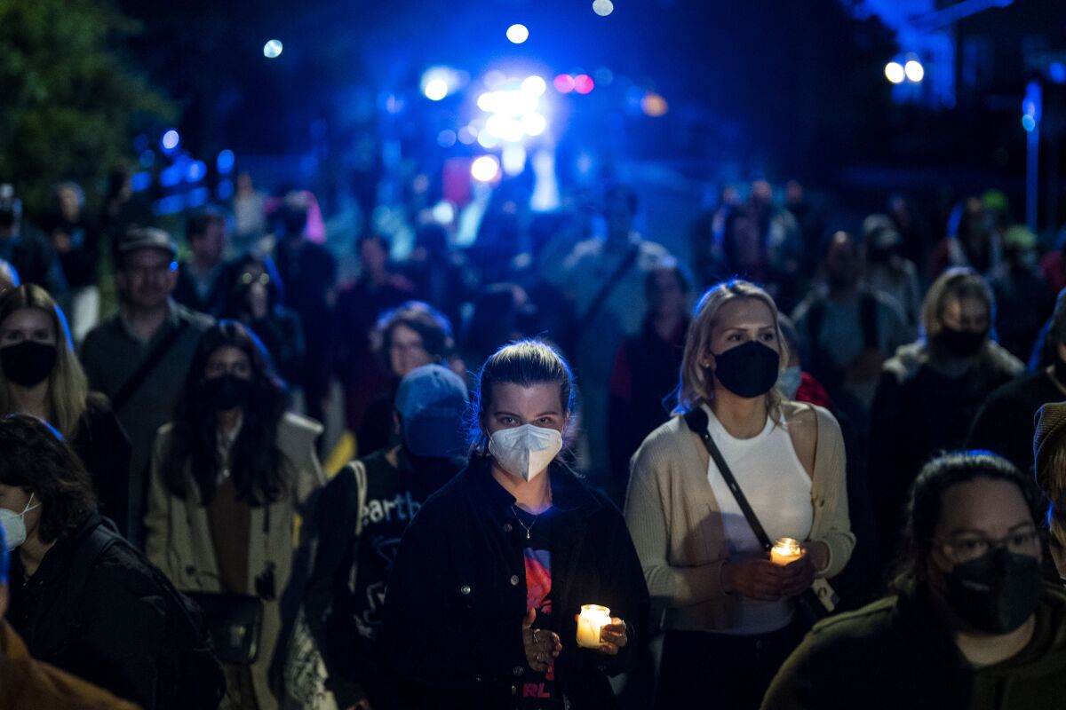 People in face masks, many of them women, stand in a group holding lighted candles after dark.