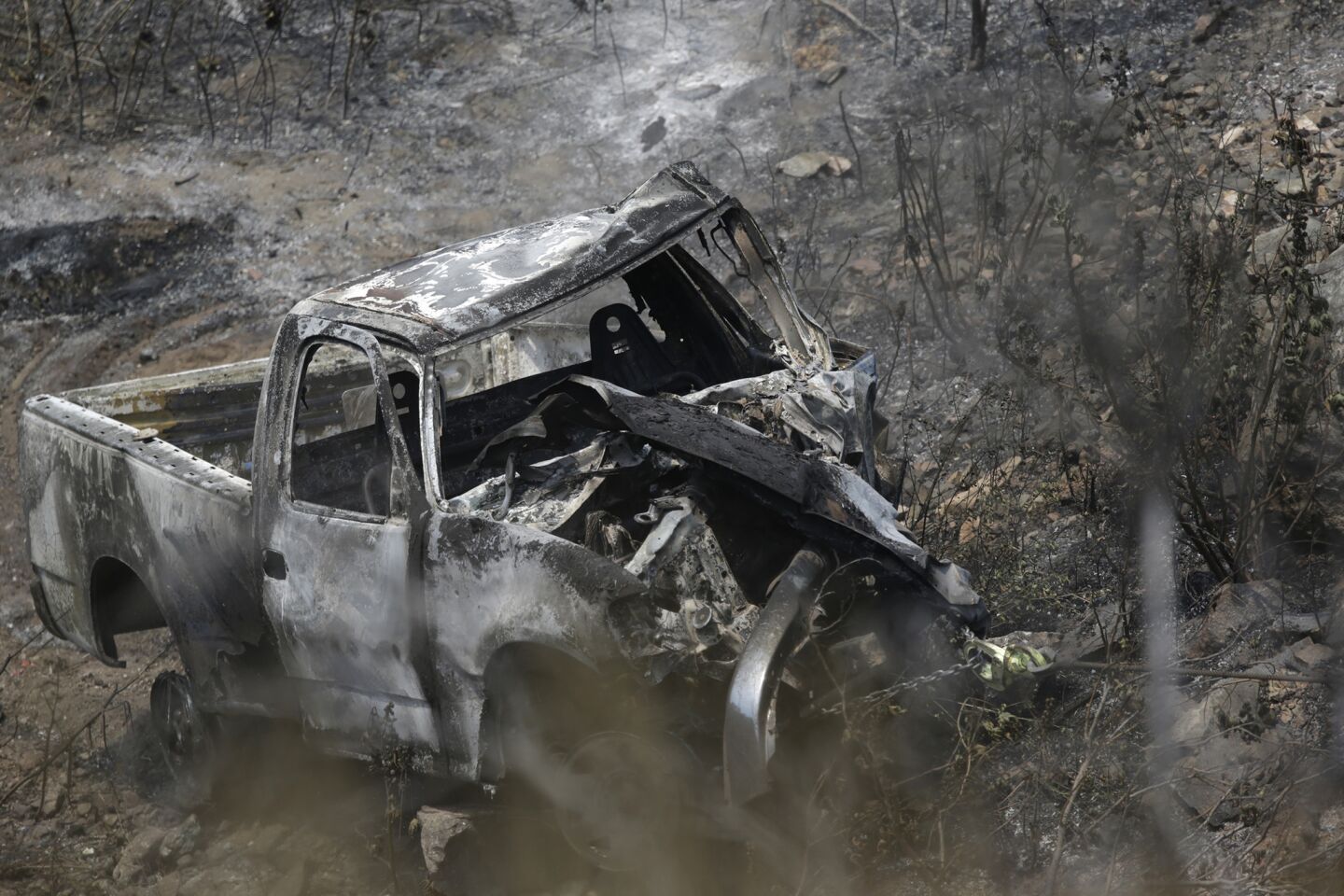 The charred and battered remains of a truck are dragged uphill near the Morris reservoir a day after it crashed and started the Reservoir Fire near Azusa.