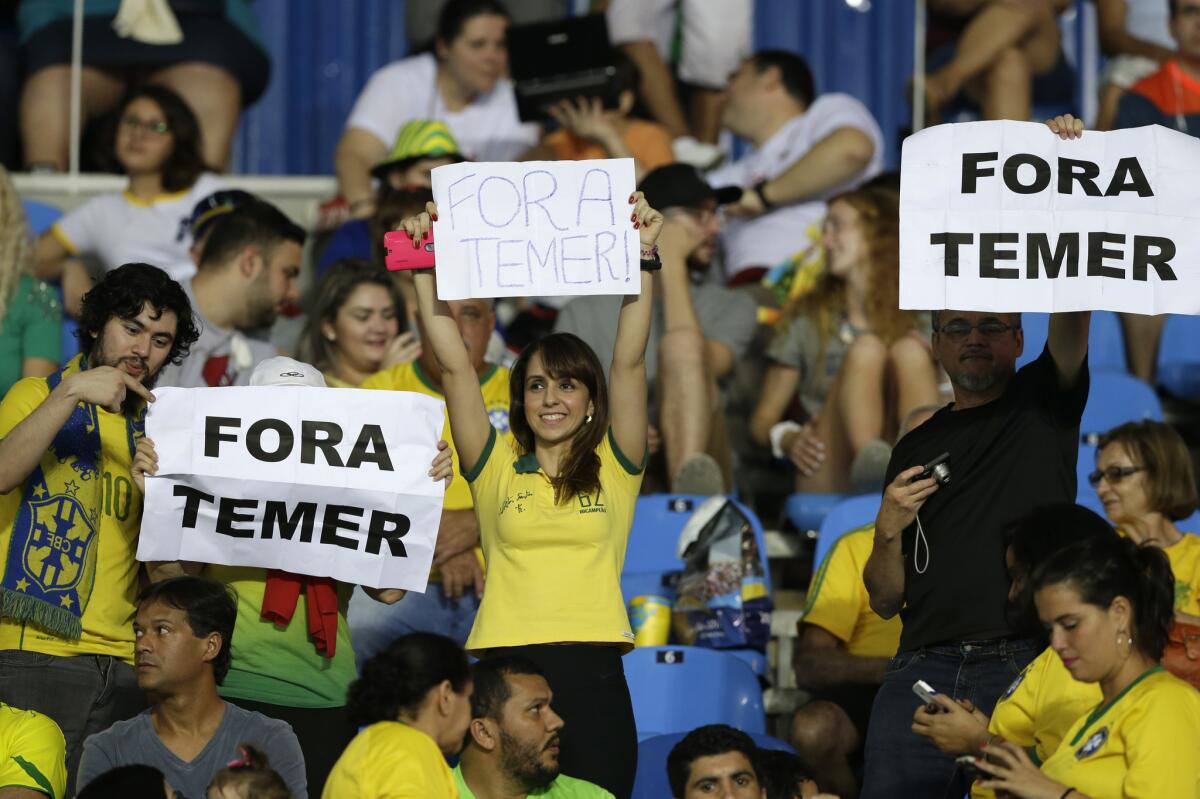 In this Aug. 6, 2016 photo, fans hold signs that read in Portuguese; "Temer Out" prior to a group E match of the women's Olympic football tournament between Brazil and Sweden at the Rio Olympic Stadium in Rio de Janeiro, Brazil. A court ruling banning the removal of protesters from Olympic venues is fueling debate on whether Brazil's political crisis should be kept out of the athletic competition. The ruling Monday came after a Brazilian Olympic volunteer defaced his official credentials to demonstrate his opposition to orders to escort out of stadiums fans holding up signs against interim President Michel Temer. (AP Photo/Leo Correa)