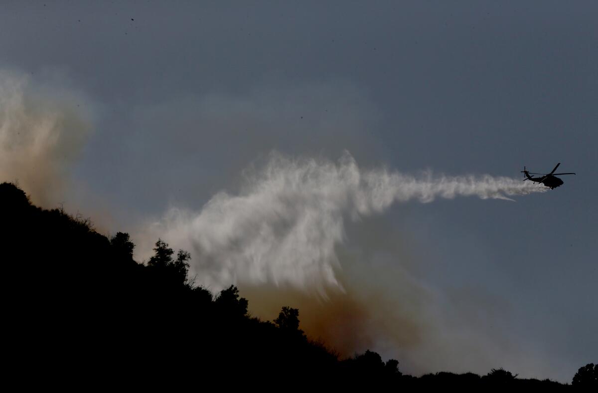 A firefighting helicopter makes a water drop on a brush fire in the hills above Ed Davis Park in Newhall 