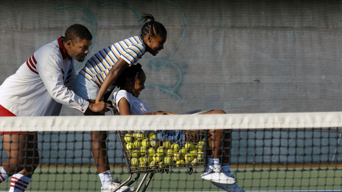 Will Smith as Richard Williams pushes his daughters in a shopping cart filled with tennis balls on a tennis court.