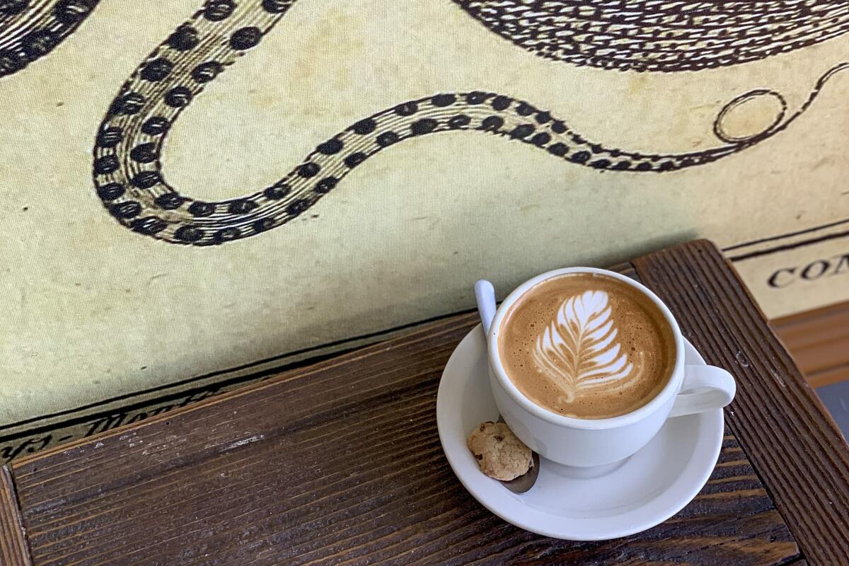 A cup of coffee sits on a table next to a wall decorated with a tentacle.
