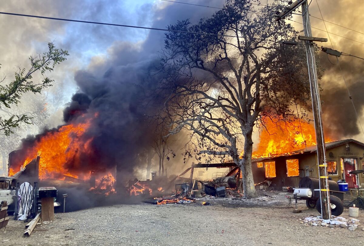 Flames consume a home and other structures as black smoke rises from the fire