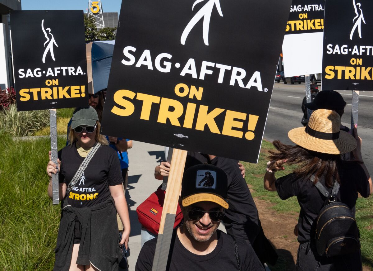 People outdoors carrying picket signs that read "SAG-AFTRA on strike!"