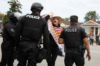 Officers in riot gear confront a protester wearing a sun hat and serape