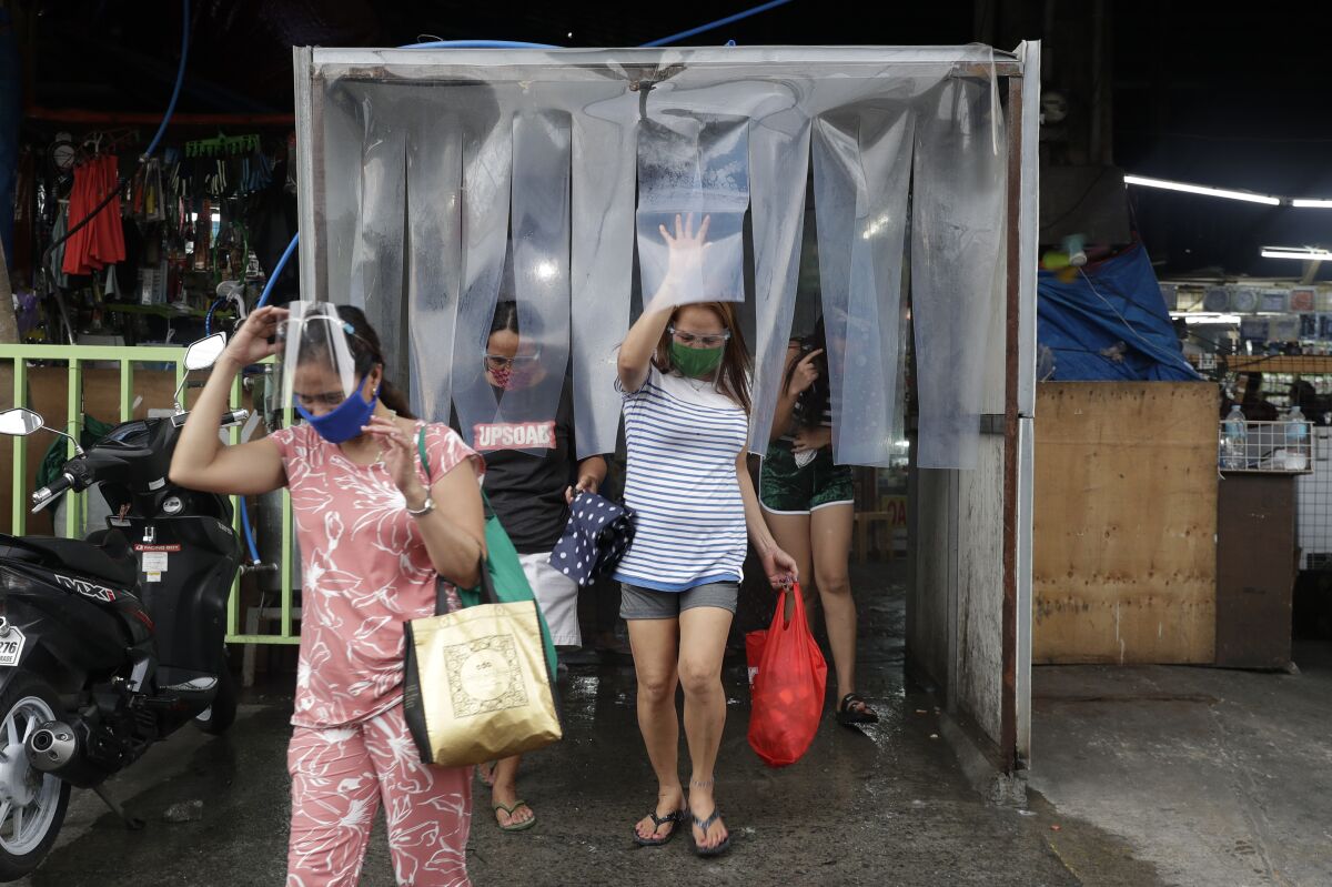 Women exit from a disinfecting area after buying food at a public market in preparation for stricter lockdown measures in Quezon city, Philippines on Monday, Aug. 3, 2020. Philippine President Rodrigo Duterte is reimposing a moderate lockdown in the capital and outlying provinces after medical groups appealed for the move as coronavirus infections surge alarmingly. (AP Photo/Aaron Favila)