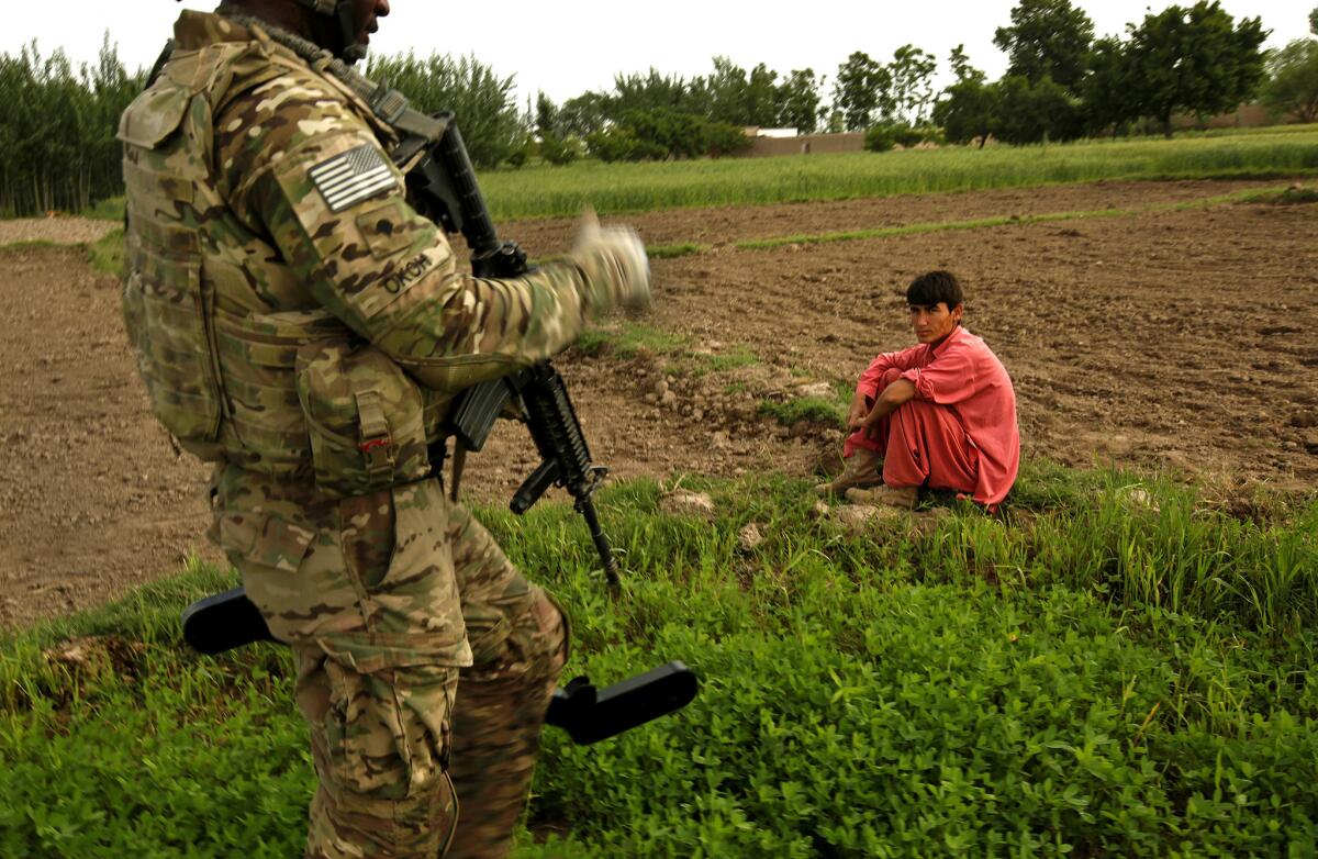An Afghan farmer waits as Spc. Uche Okoh uses a mine detector to sweep an area.