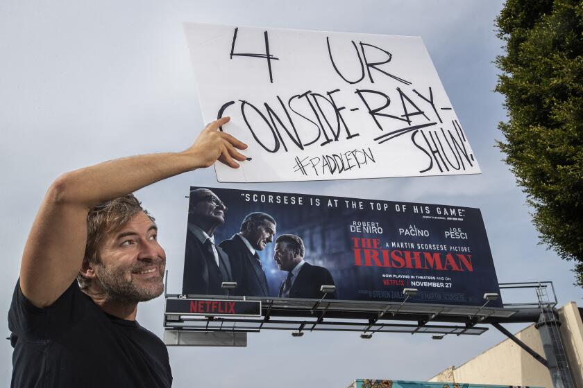 LOS ANGELES, CA-NOVEMBER 15, 2019: Actor Mark Duplass holds a sign above a billboard on Sunset Blvd, along the Sunset Strip in Los Angeles, promoting the movie, The Irishman, as he conducts a one-man awards campaign for his “Paddleton” co-star Ray Romano on November 15, 2019. Romano appeared in The Irishman. (Mel Melcon/Los Angeles Times)