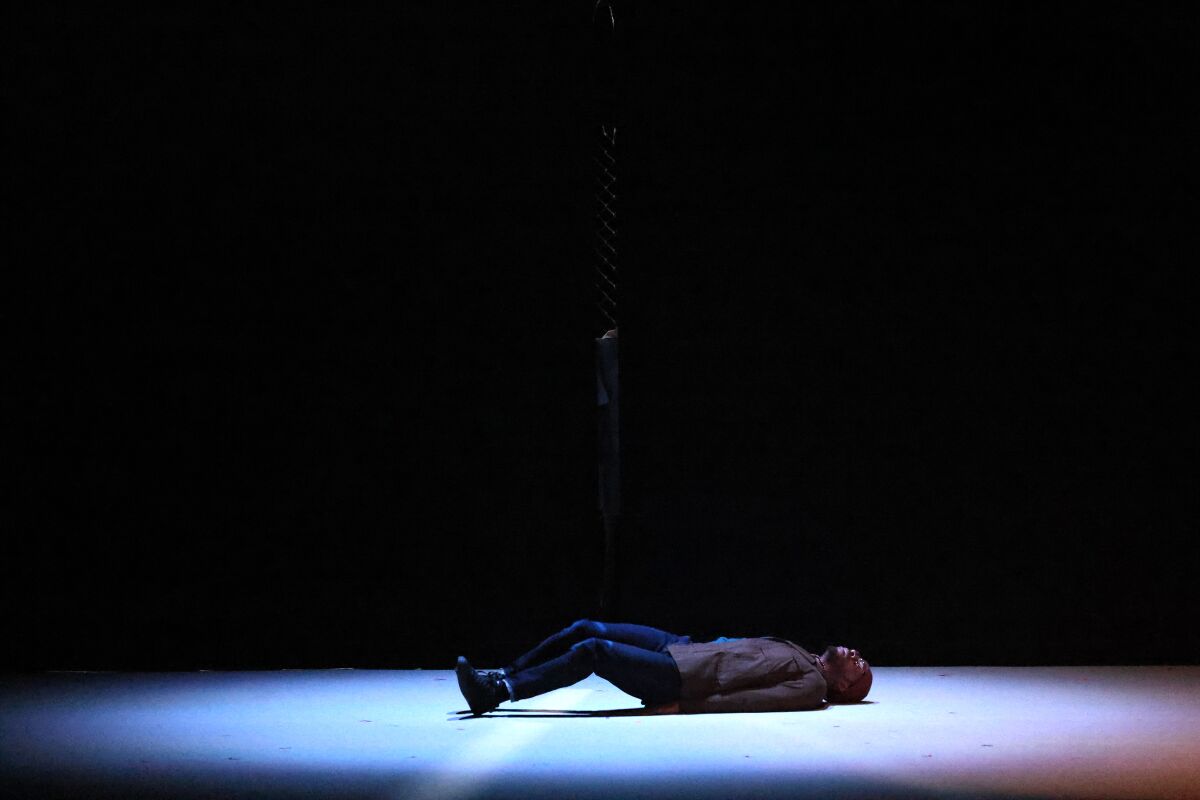 A man lies in a pool of white light onstage during a performance of "Fidelio." 