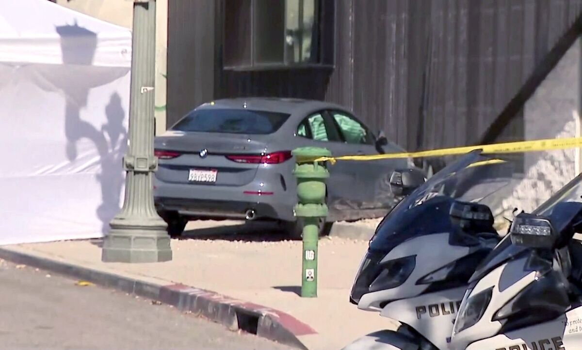 A car rests on the sidewalk after crashing into a building. 