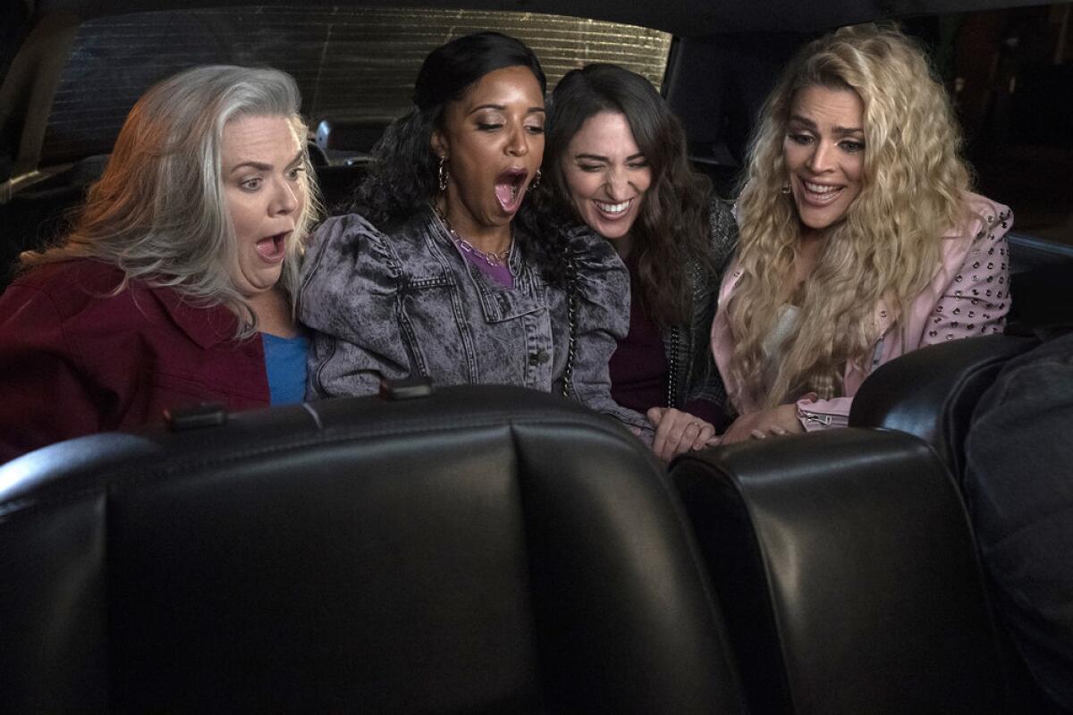 Four women appear surprised by something in the back of a limousine.