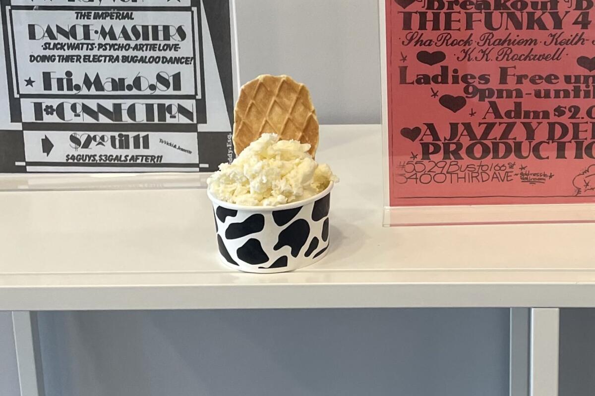 A cup of ice cream with a cookie perched on top sits on a counter with event posters