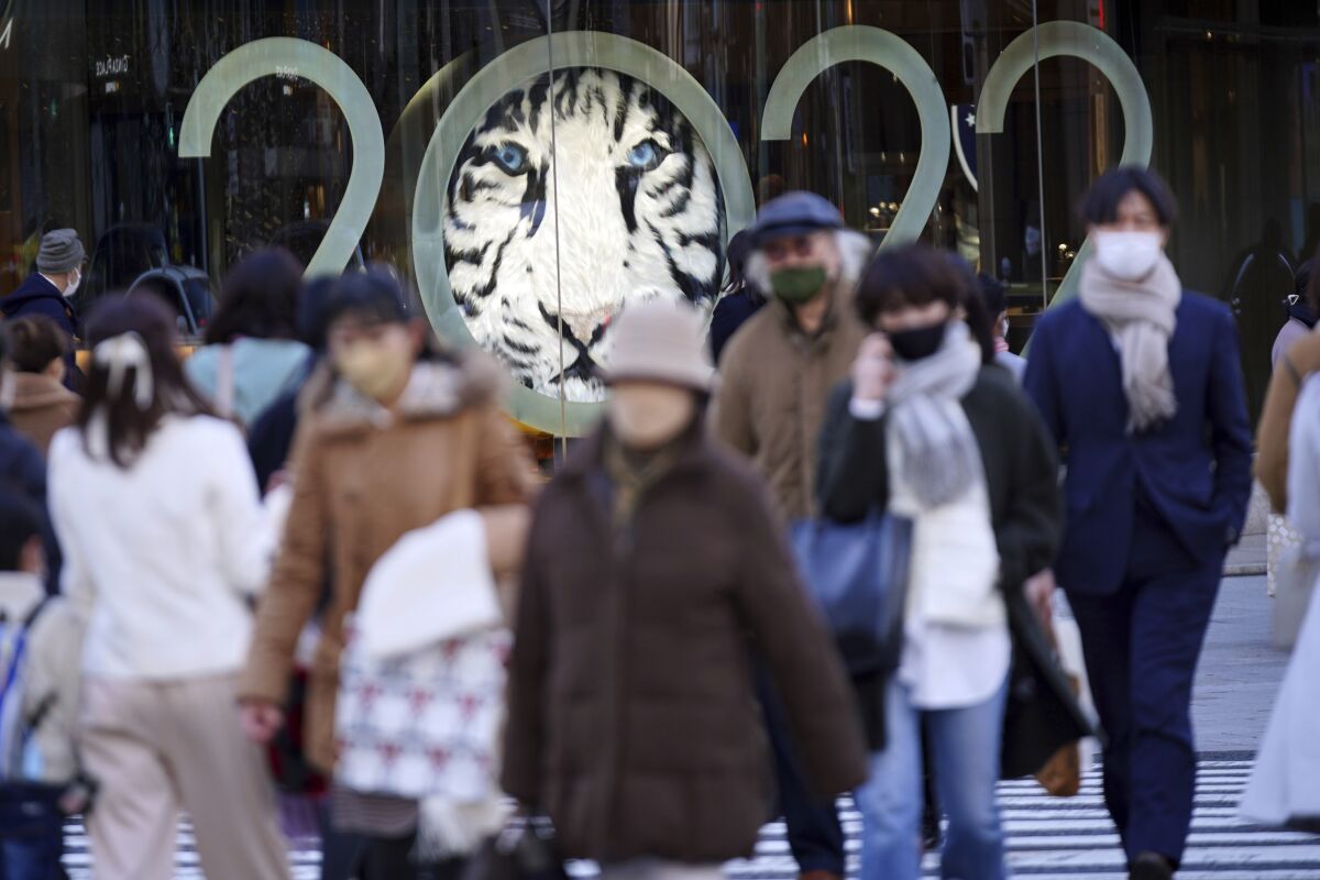 People wearing protective masks to help curb the spread of the coronavirus walk along a pedestrian crossing Tuesday, Jan. 18, 2022, in Tokyo. Japan's government is preparing social restrictions in Tokyo and other regions as the omicron variant of the coronavirus infects more people. (AP Photo/Eugene Hoshiko)