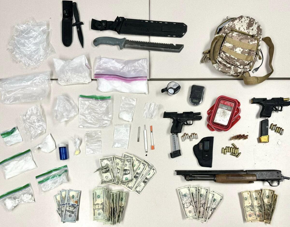 A display on a flat surface of weapons, cash, a small backpack, and pills and substances in baggies.