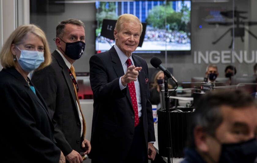 Bill Nelson stands while pointing, alongside two other people in an office space. 