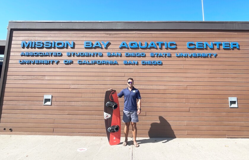 Andrew Fineman poses with a board in front of the Mission Bay Aquatic Center.