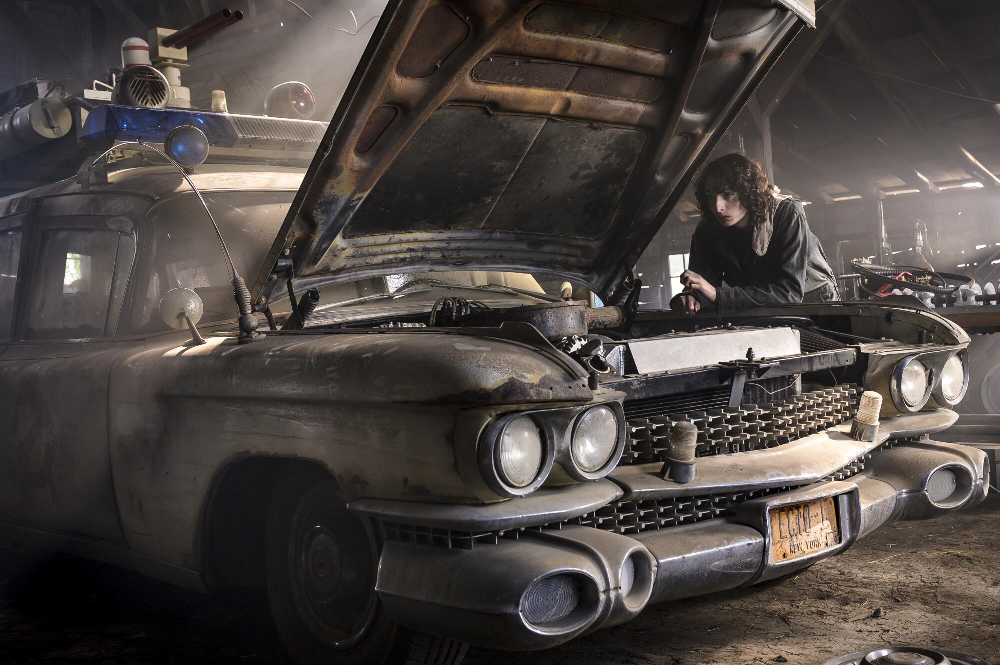 A young man leans on a car with an open hood.