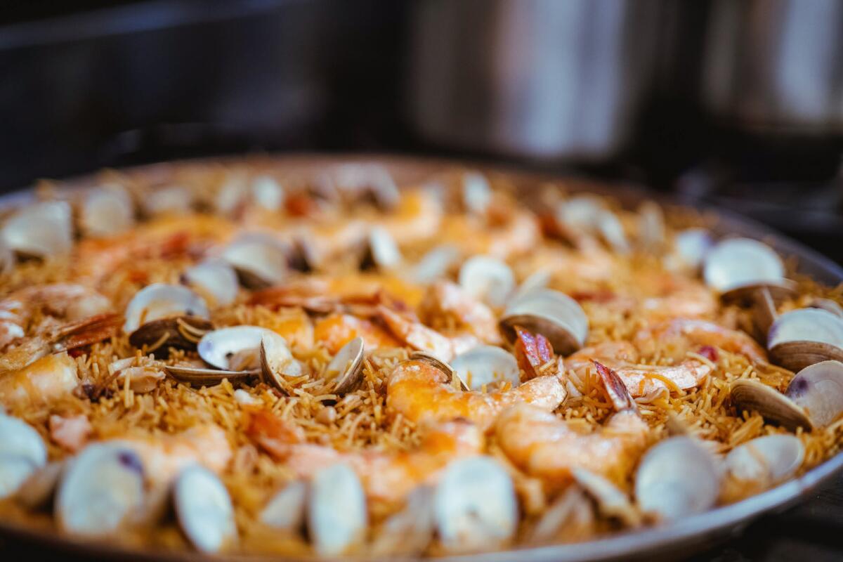 A closeup side photo of a large pan of fideus rossejat decorated with clams and shrimp.