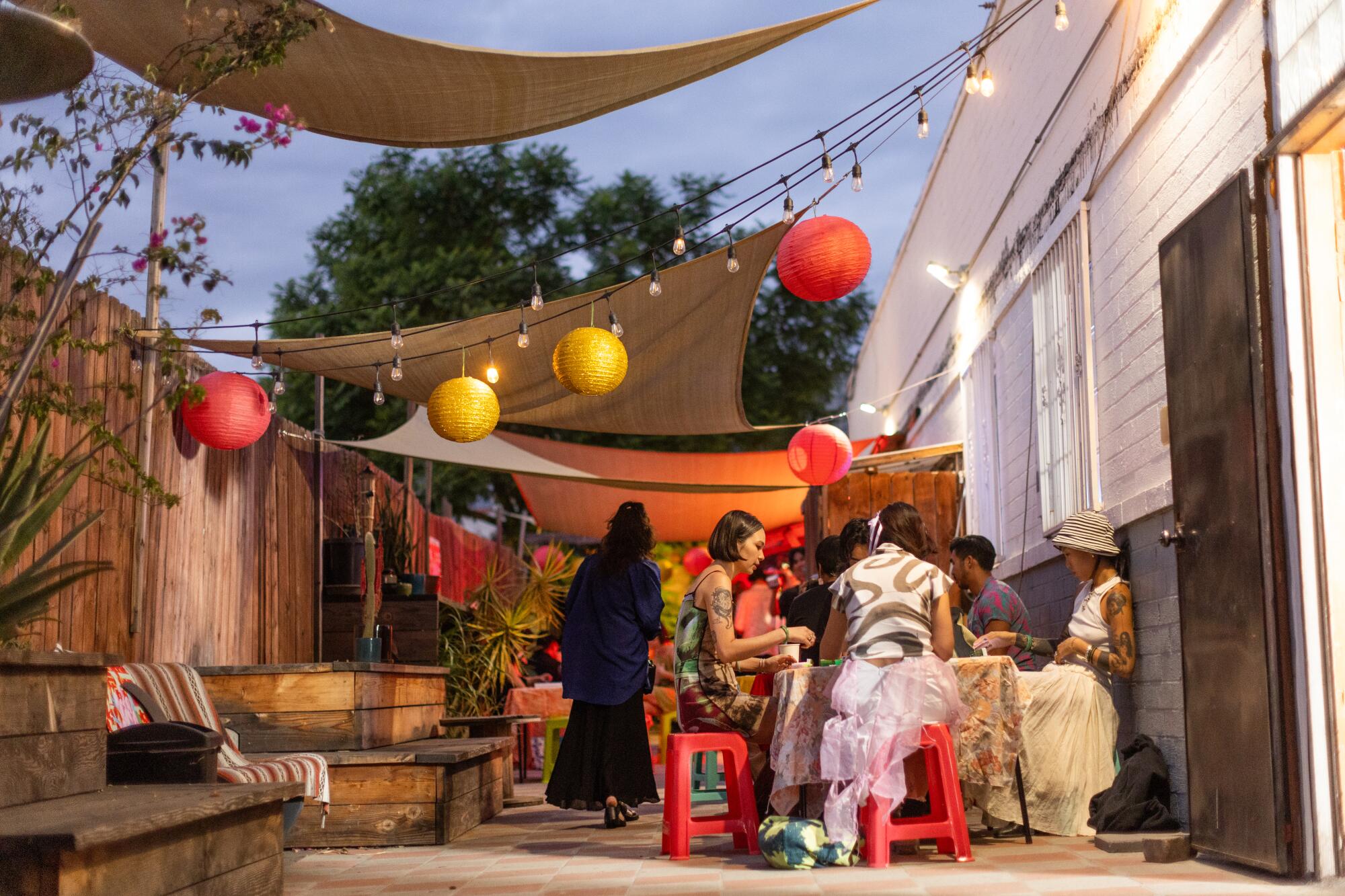 People sit at outdoor tables under shade sails and paper lanterns