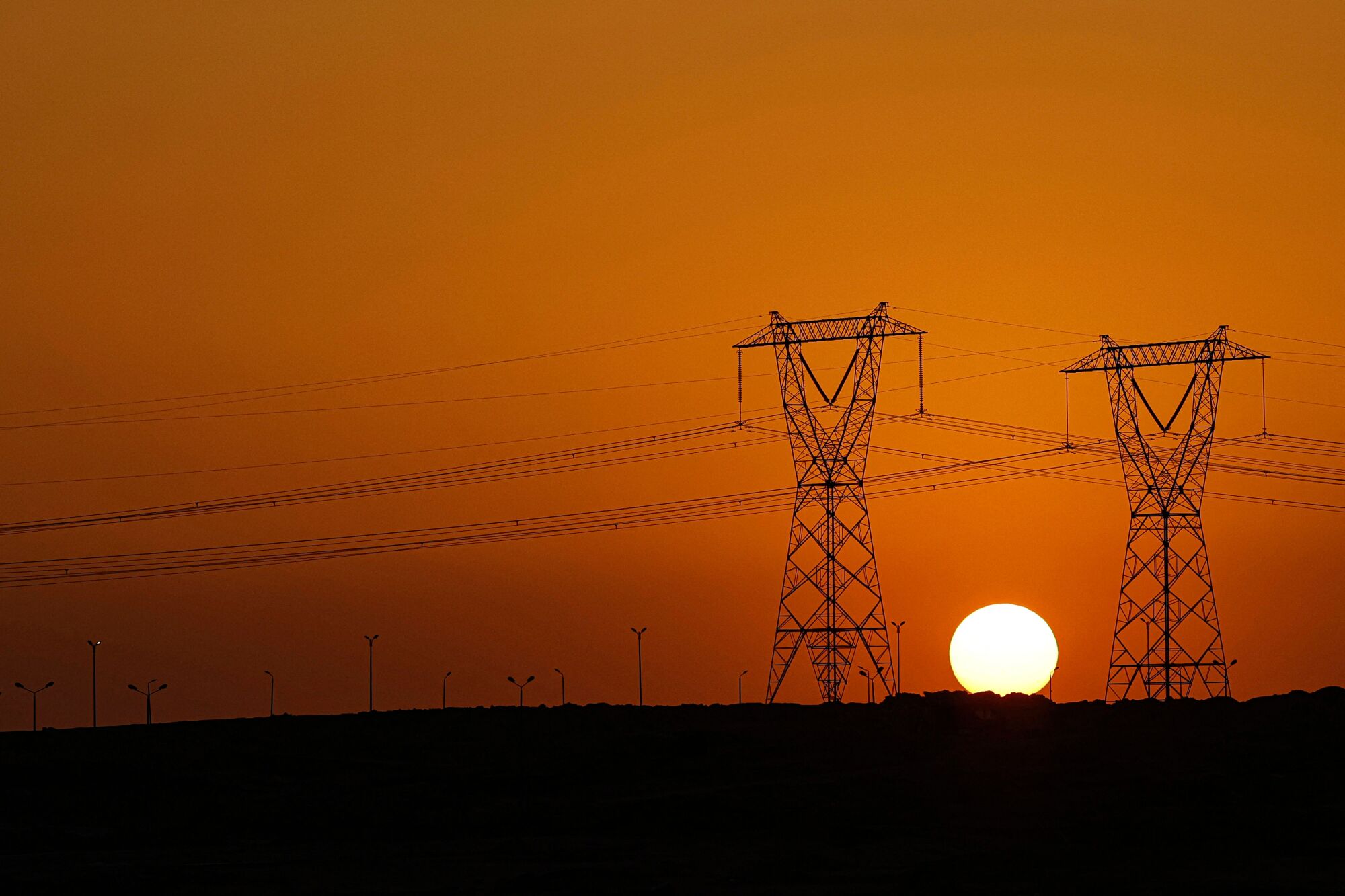 Sun setting behind electricity pylons against orange skies 