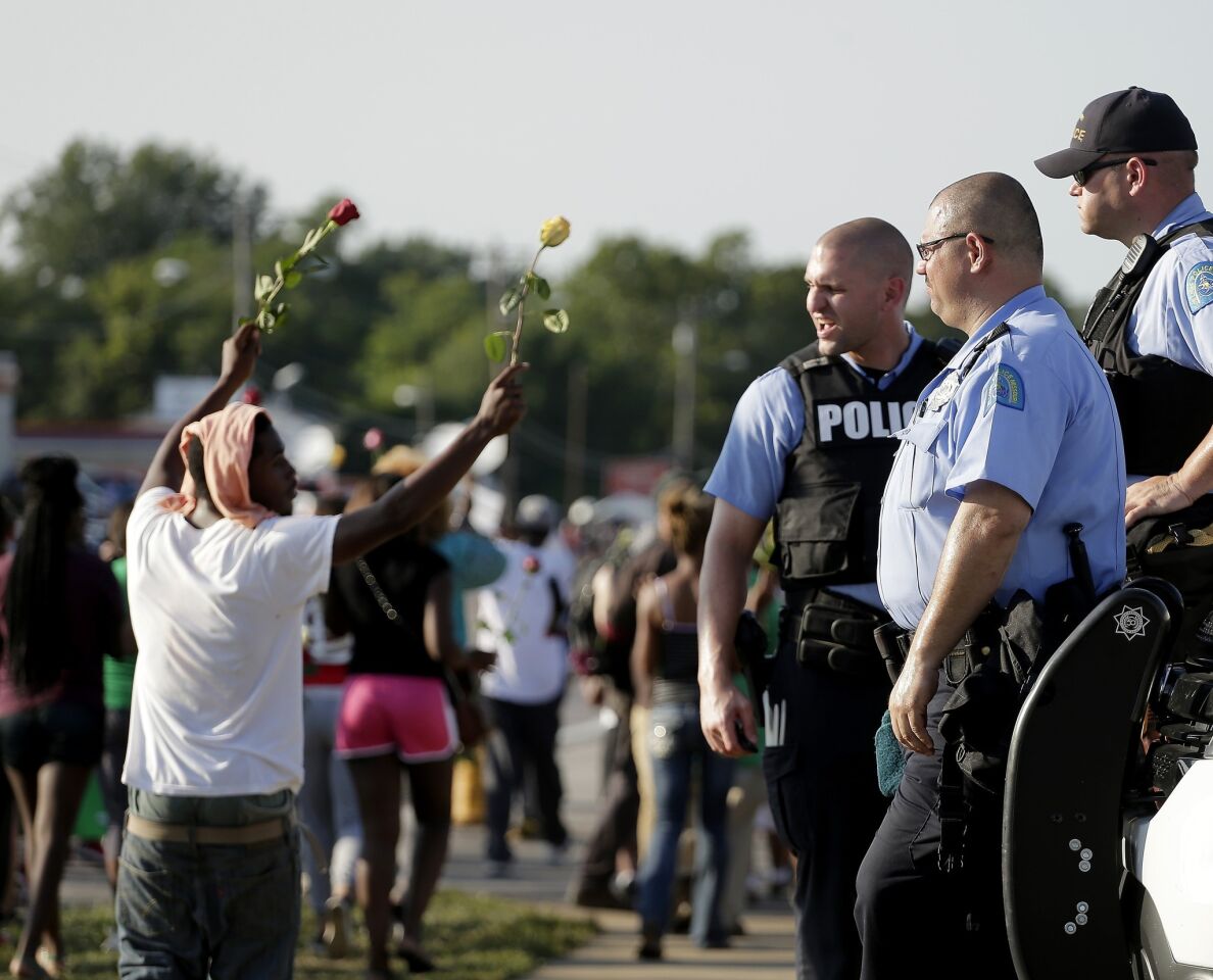 Demonstrators in Ferguson march as police look on.