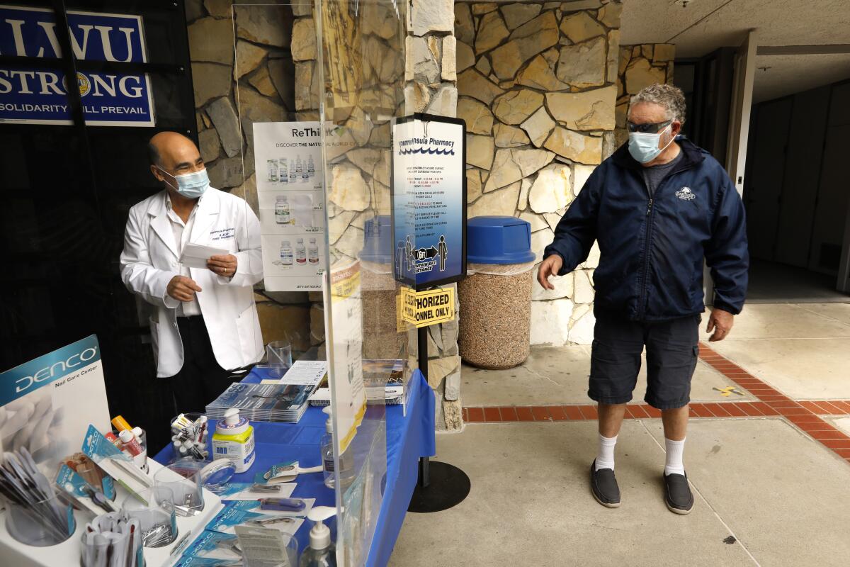 Chief pharmacist Shahram Elie, right, wears a double mask when serving customers at Peninsula Pharmacy in San Pedro