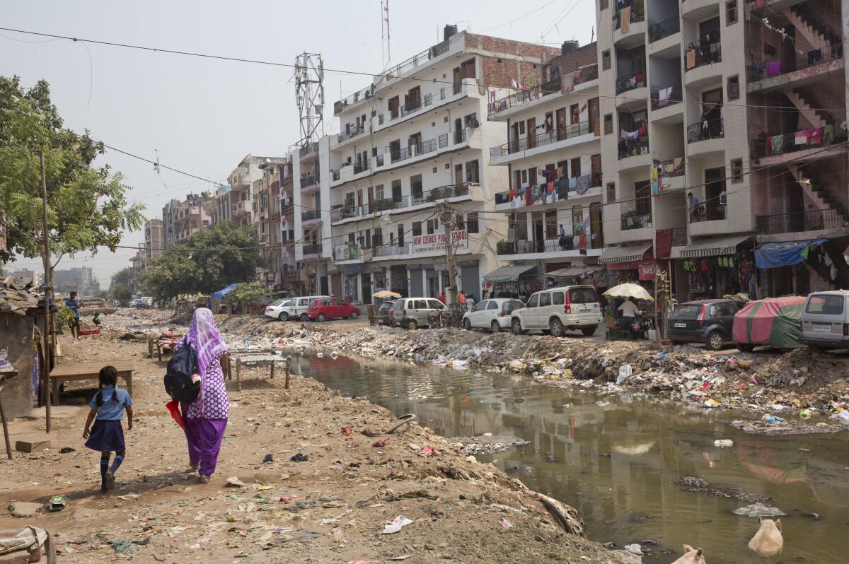 A woman and child walk beside stagnant water in front of an apartment building