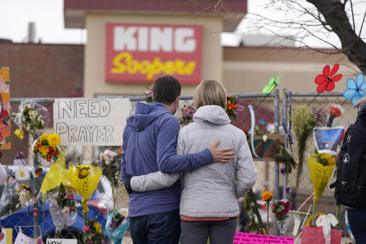 A couple stands by a fence covered with memorial cards and flowers outside the King Soopers store.