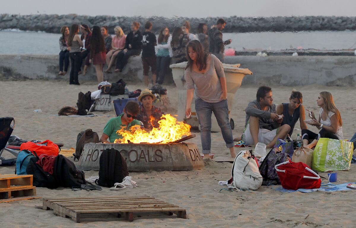 Friends huddle around a fire pit at Big Corona State Beach in Corona del Mar.