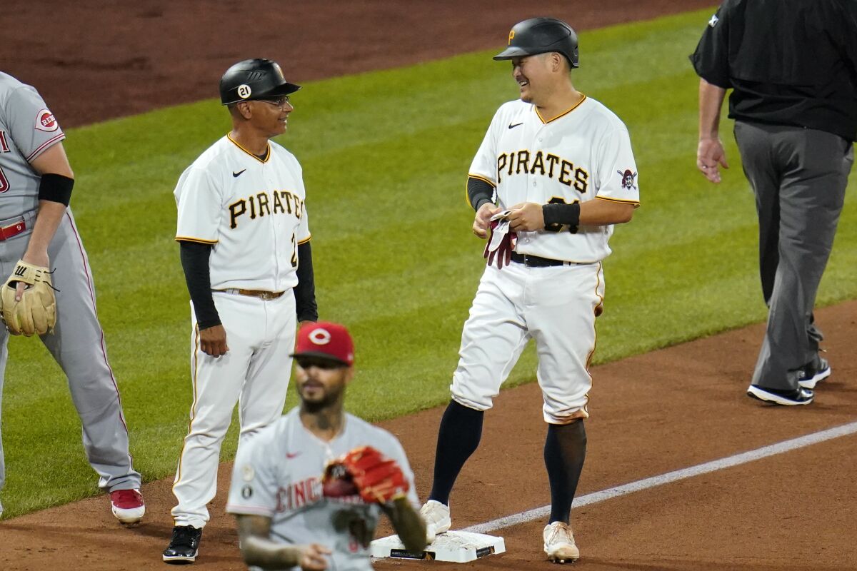 Pittsburgh Pirates' Yoshi Tsutsugo, right, stands on third, talking with coach Joey Cora, left, after hitting an RBI double and advancing on an error during the third inning of the team's baseball game against the Cincinnati Reds on Wednesday, Sept. 15, 2021, in Pittsburgh. (AP Photo/Gene J. Puskar)