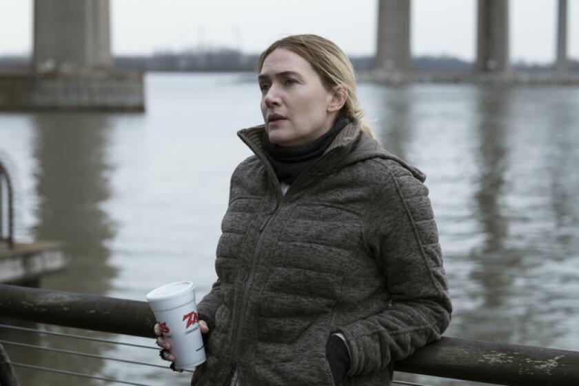 A woman in a winter coat holding a styrofoam cup and leaning on the railing beside a river