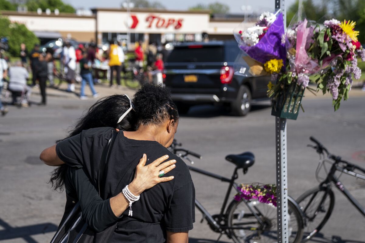 Two people embrace next to a memorial with flowers outside a Tops store
