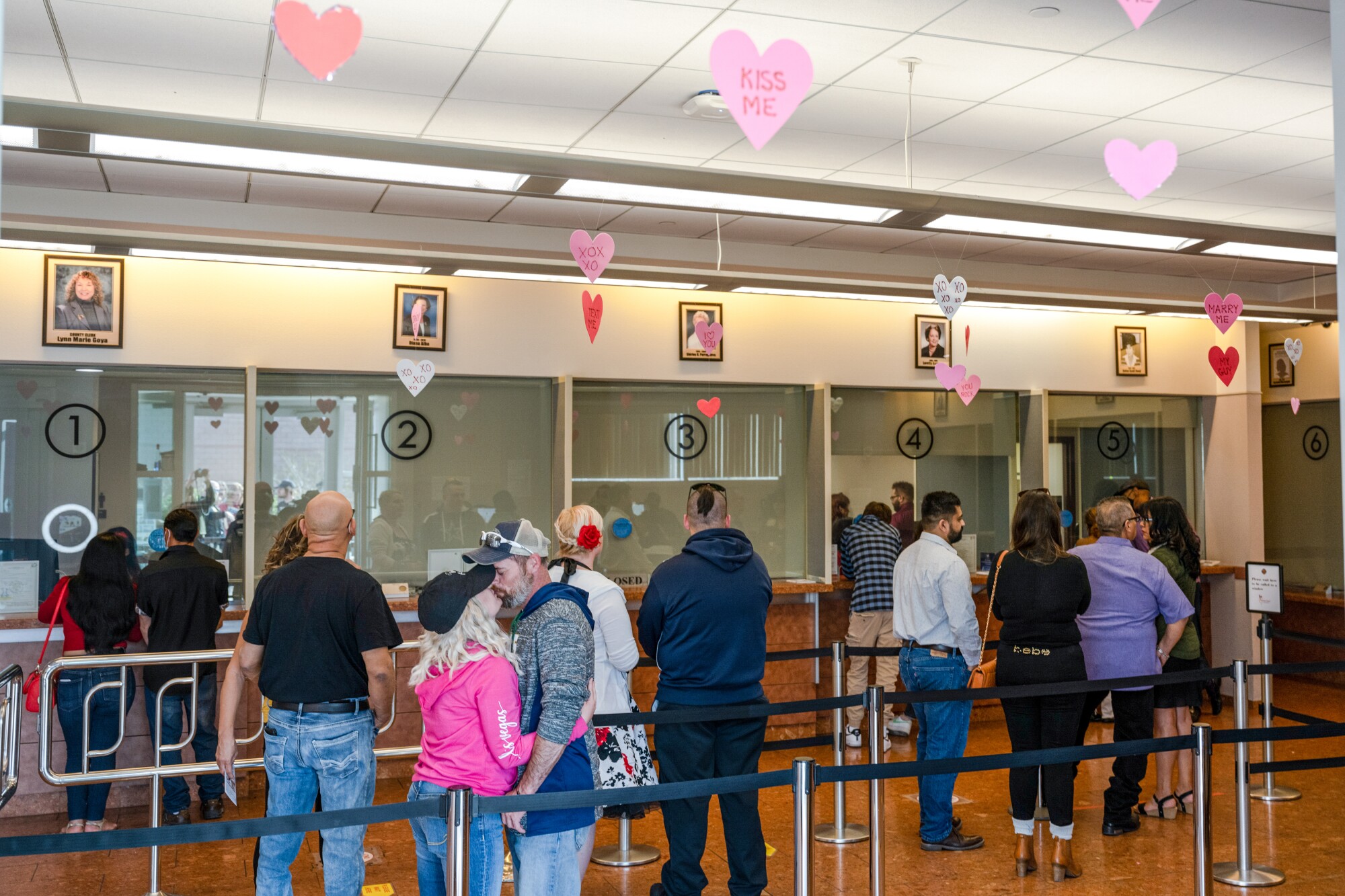 Couples wait in a line at a government office decorated with hearts 