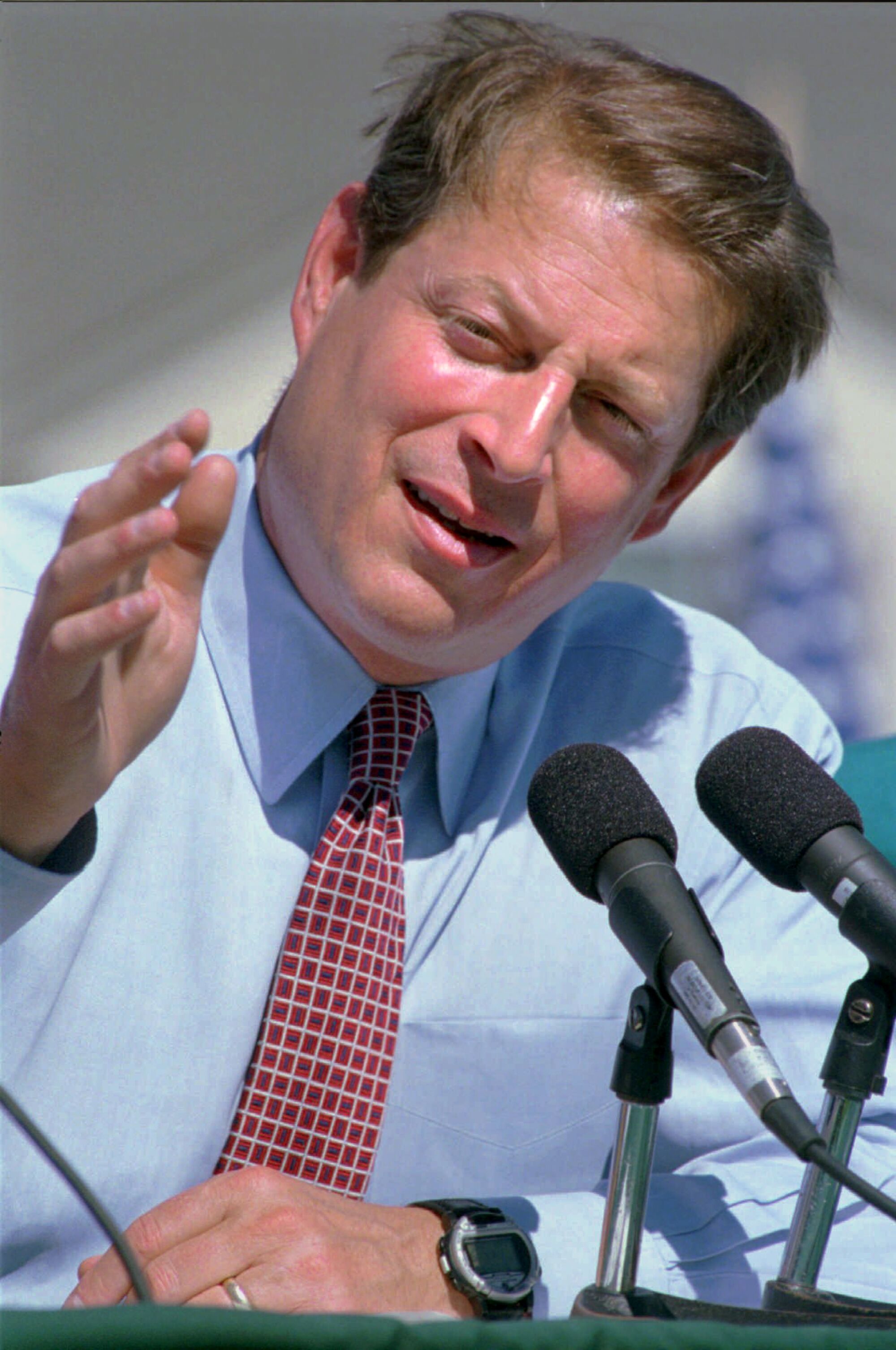 Un cadre vertical tête-et-épaules d'Al Gore devant des microphones, faisant des gestes avec son bras droit