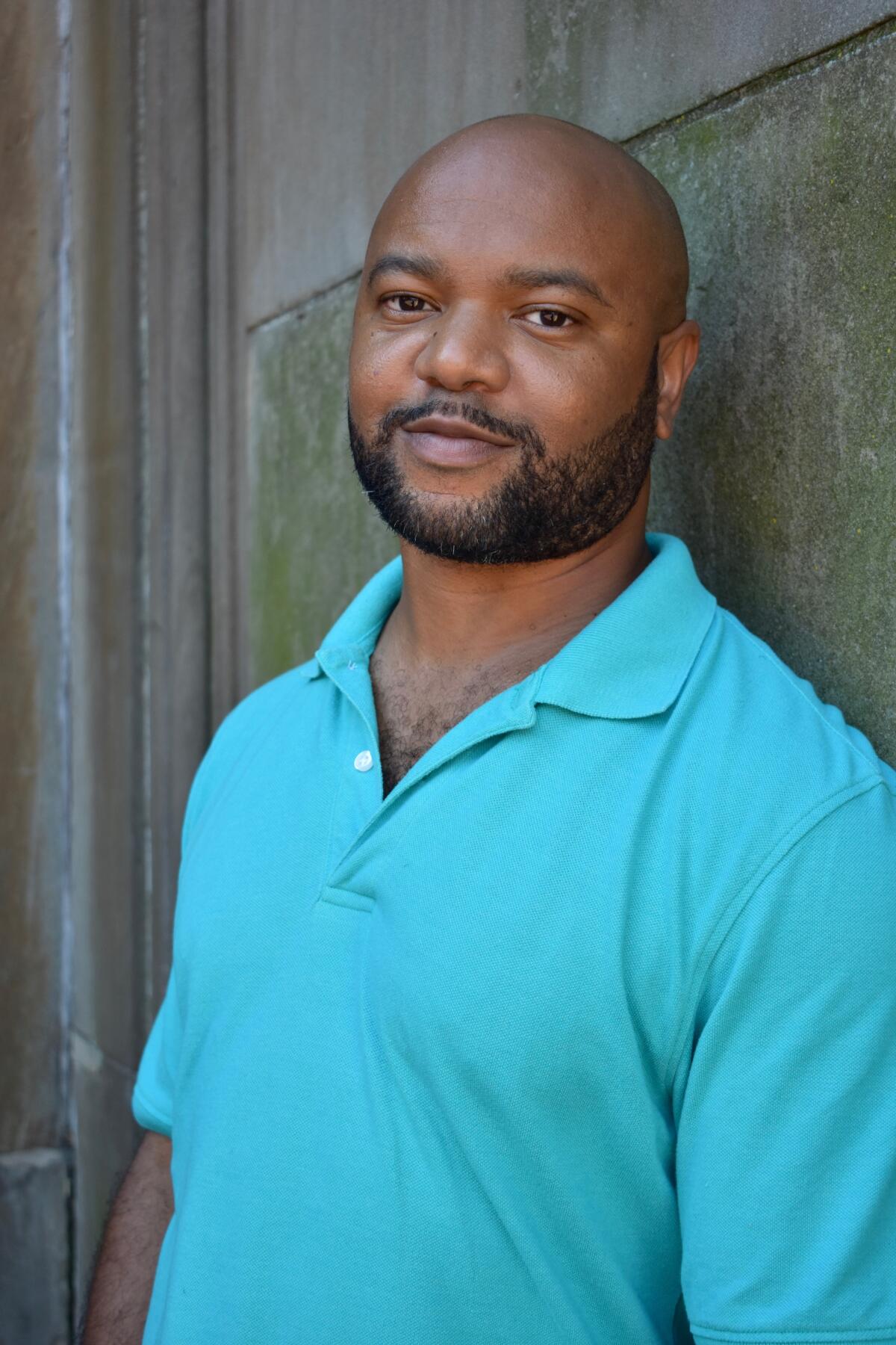 De'Shawn Charles Winslow, wearing a blue polo shirt, leans against a wall.