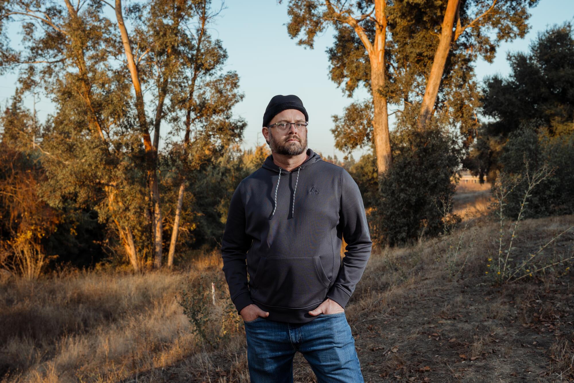 A man stands in a grassy area near a group of trees