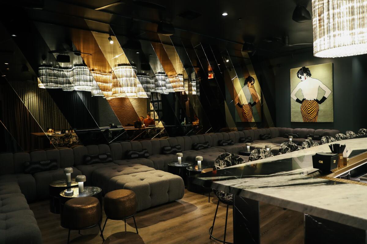 A modern-looking dark bar interior with a large, wavy statement chandelier to the left side.